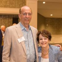Guests at Naples 2019. A man is standing next to a sitting woman, and he has his arm around her.